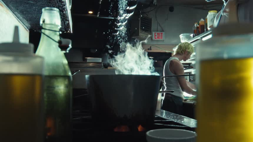 A chef seasons a steaming pot on a stove in a professional kitchen, filmed in dramatic slow motion