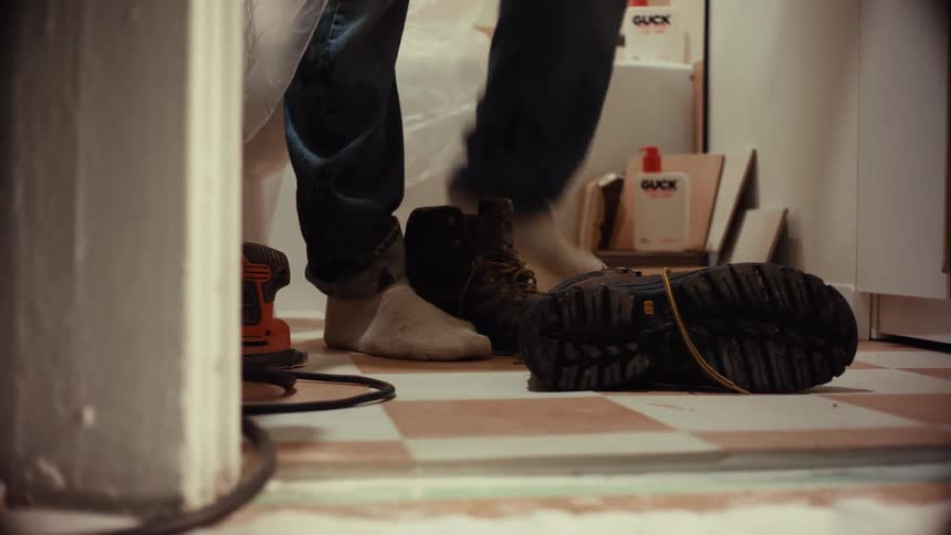 A low angle shot of a construction worker in jeans taking off their dirty work boot inside a bathroom under renovation