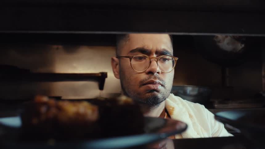 View from the serving window as a focused chef lines up finished plates of food in a bustling restaurant kitchen