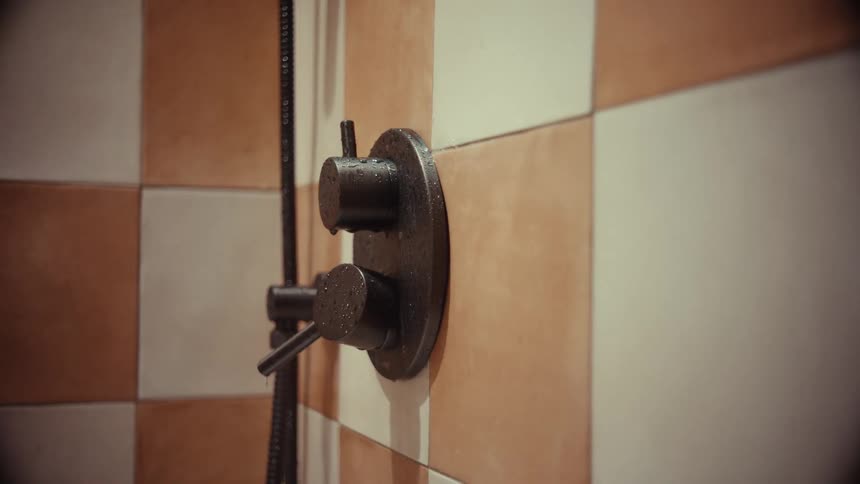 A close-up shot of a man's hand turning on a black shower faucet and testing the water temperature