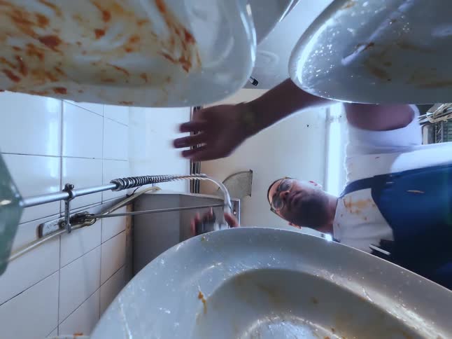 A point-of-view shot from inside a commercial sink as a worker rinses dirty plates with a high-pressure sprayer