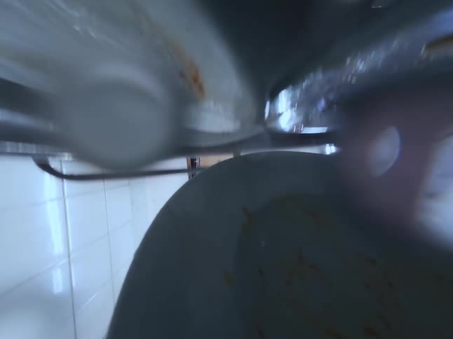 A point-of-view shot from inside a commercial sink as a worker rinses dirty plates with a high-pressure sprayer