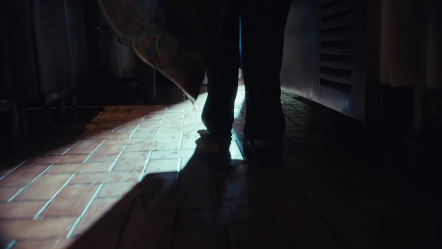 Low-angle slow-motion shot following a person's feet as they drag a leaking garbage bag across a dark and wet kitchen floor