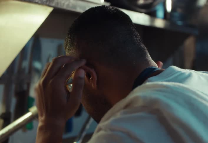 A stressed and overwhelmed professional chef holds his head in his hands, feeling the pressure of the restaurant kitchen in slow motion