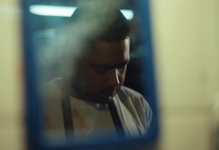 The reflection of a troubled man in an apron washing his face, which turns bloody and distorted in a dark room