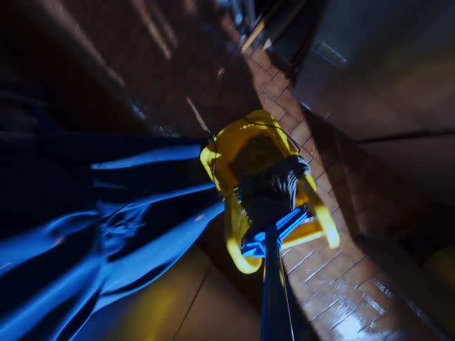 A dynamic POV shot from a mop as it's used to clean the tiled floor of a dimly lit commercial kitchen