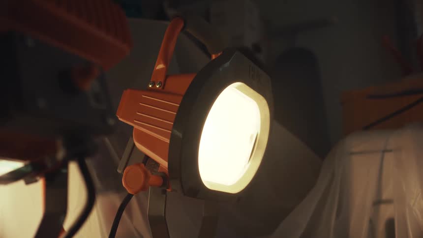 A close-up shot of a bright orange industrial work light slowly fading to black in a workshop
