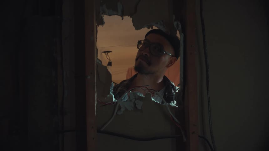 A curious man smiles as he peeks through a hole in the wall, his expression changing as he observes the other side