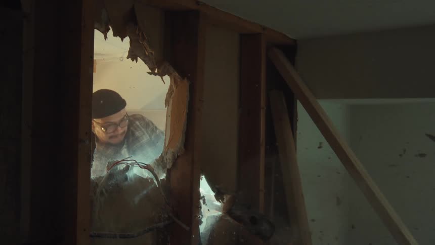A construction worker smashes through drywall with a sledgehammer in dramatic slow motion during a demolition
