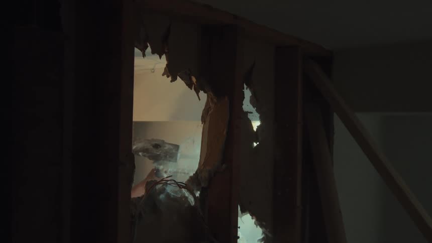 Dramatic slow-motion shot of a sledgehammer breaking through a plaster wall, creating dust and debris