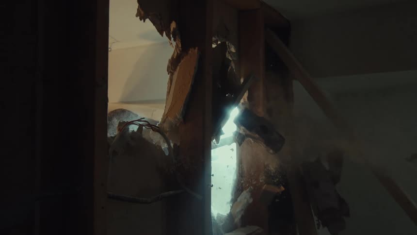 A sledgehammer smashes through drywall in dramatic slow motion, viewed from inside the wall