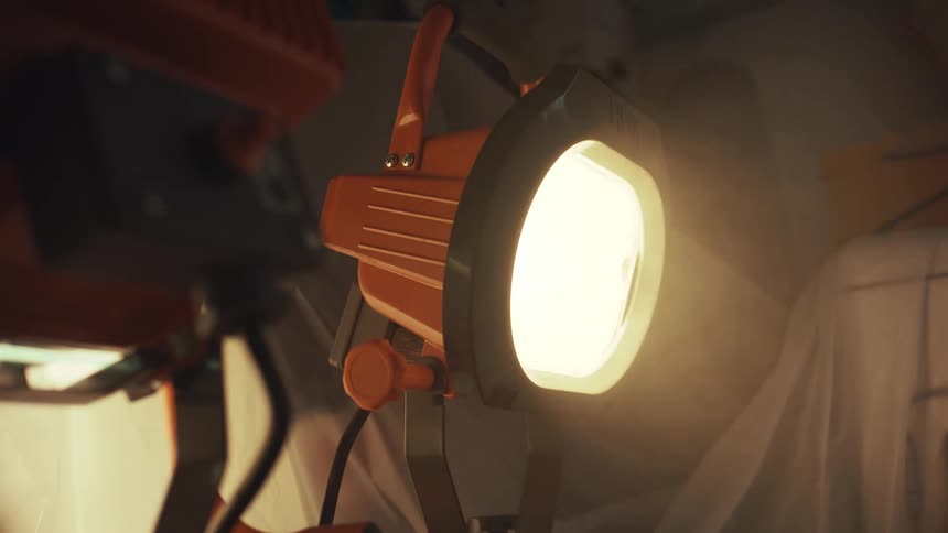 A bright orange work light flickers on and off, illuminating a dusty and dark construction site