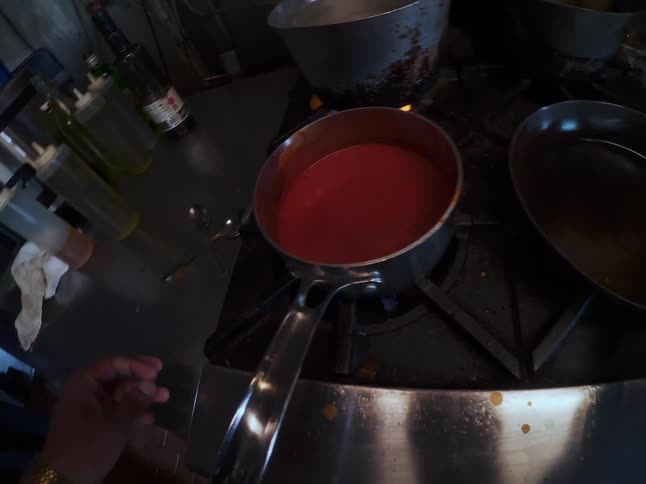 First-person perspective of a professional chef cooking, stirring a red sauce on the stove and seasoning osso buco