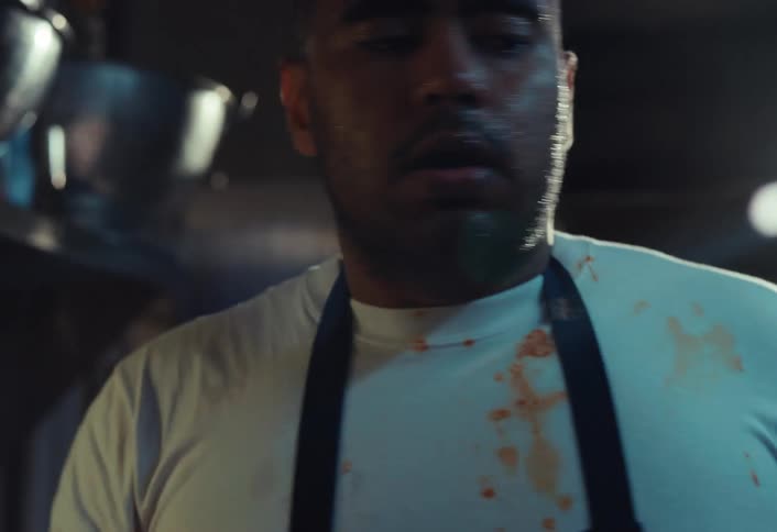 A tired chef in a professional kitchen takes a moment to cool down by splashing water on his face in slow motion
