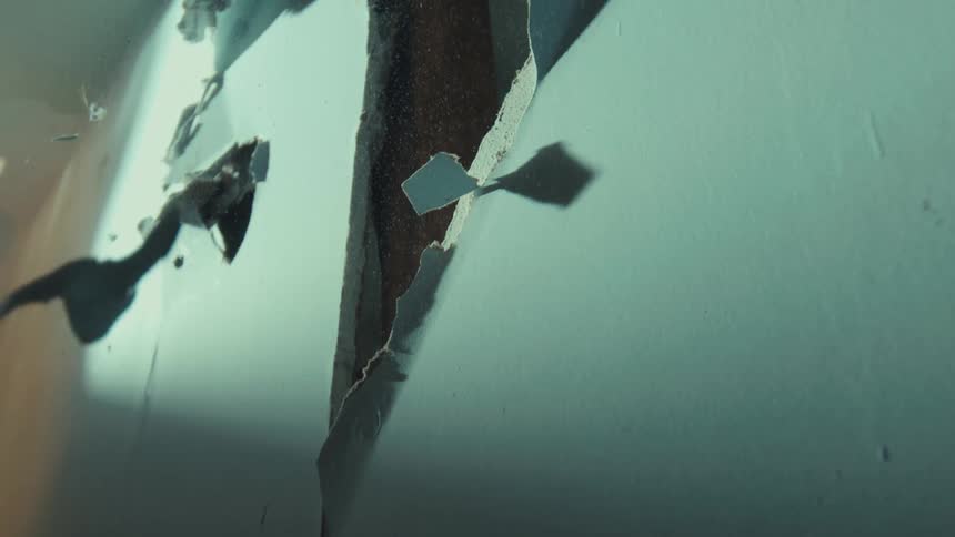 Slow motion shot of paint chips and debris falling past a cracked and decaying surface