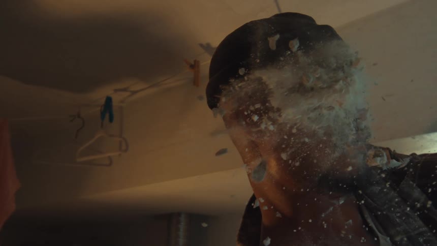 A man in a beanie and safety glasses gets hit in the face with exploding debris in a dramatic slow-motion close-up