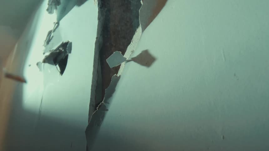 Debris and dust fall in slow motion from a hole smashed into a drywall