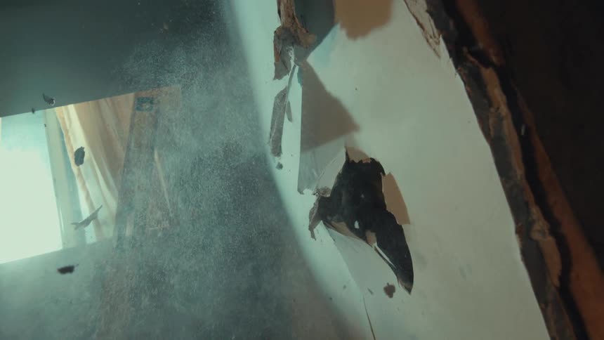 Slow motion vertical close-up of a sledgehammer smashing through drywall, sending dust and debris flying