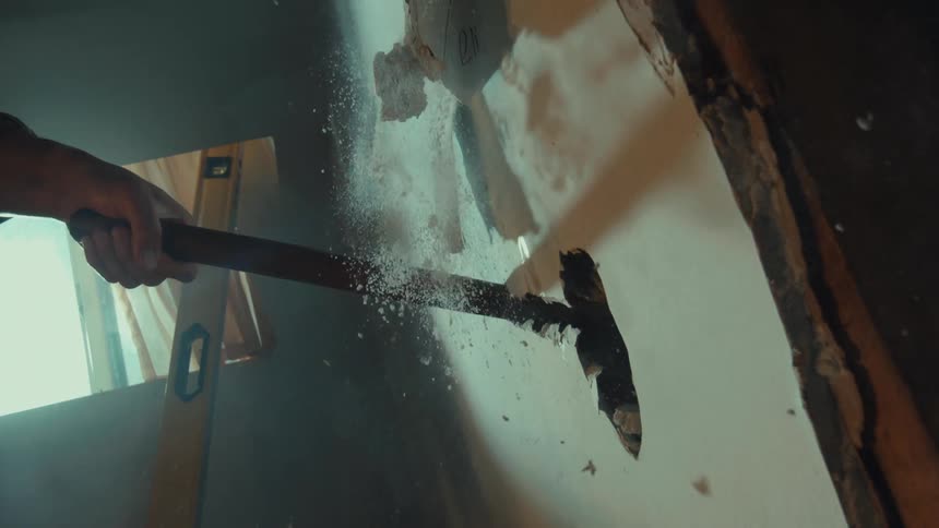 Vertical slow-motion shot of a sledgehammer smashing through a drywall wall, creating an explosion of dust and debris on impact