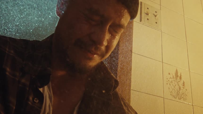 A man overwhelmed with grief weeps in the shower in dramatic slow motion