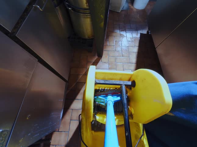 A frenetic first-person point-of-view of a mop being used to clean the tiled floor of a commercial kitchen