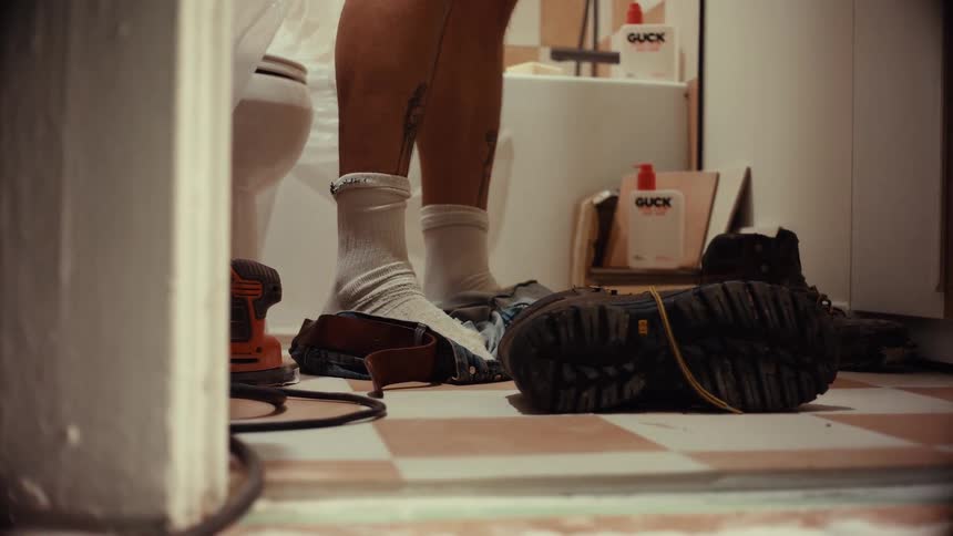 A construction worker takes off his dirty work jeans and boots in a bathroom that is under renovation