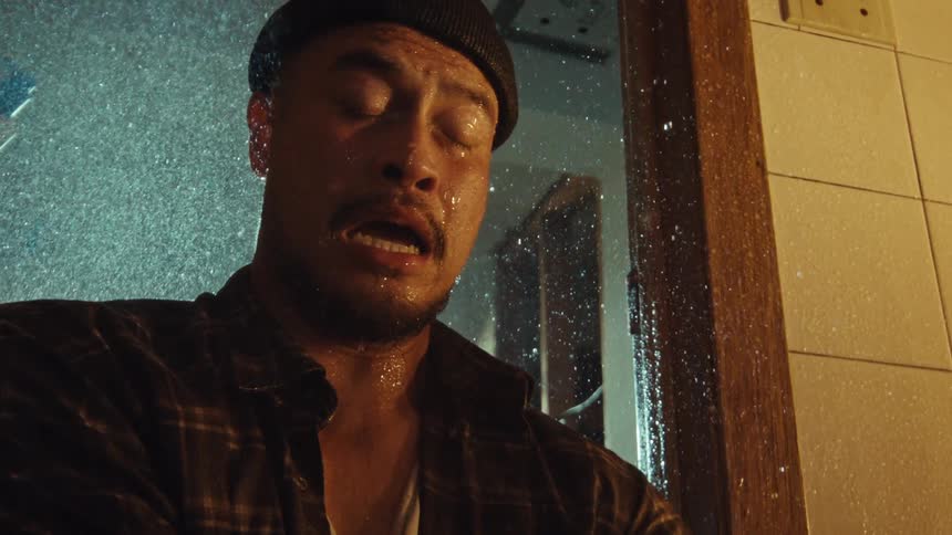 Slow motion close-up of a distraught and heartbroken man crying in agony while standing fully clothed in a cold shower