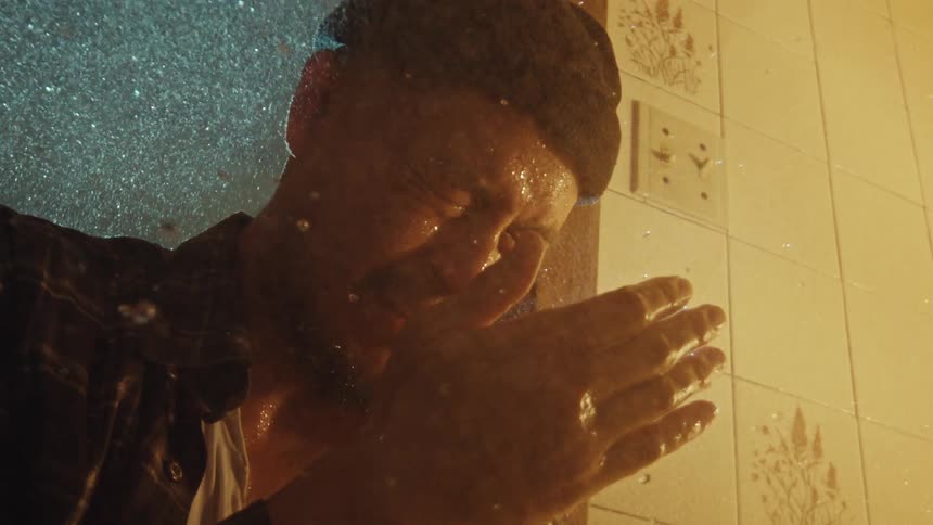 Slow motion shot of a heartbroken man crying under the falling water in a shower