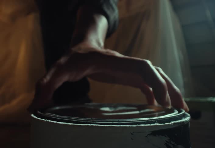A close-up shot of a hand carefully closing the lid on a can of paint in a dimly lit room