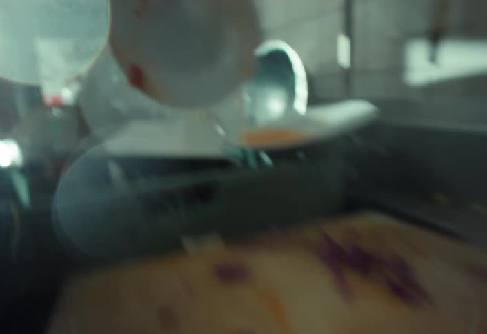A restaurant worker scrapes leftover food from a plate into a bin and then rinses it with a water sprayer