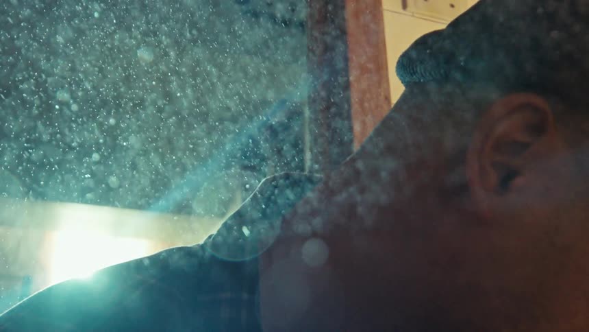 Dust particles fall in slow motion, accumulating on a mirror and obscuring the solemn reflection of a man's face