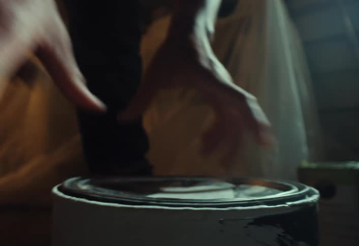 A person seals a paint can by firmly pressing the lid closed in a dimly lit room during a renovation