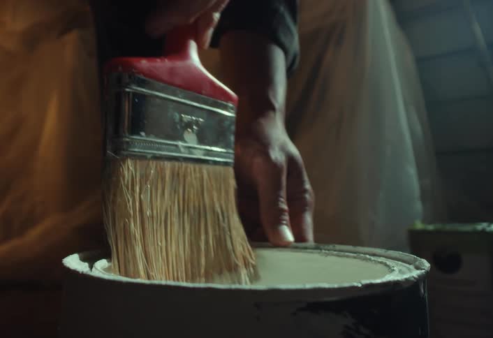 A close-up slow-motion shot of a painter dipping a paintbrush into a can of white paint