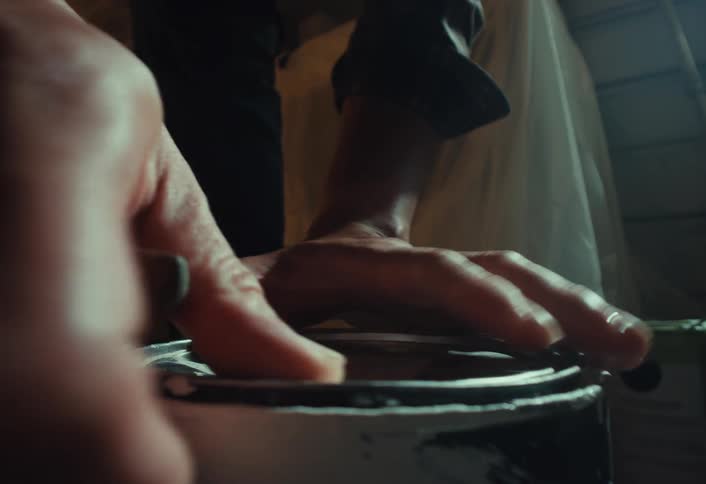 A person's hands firmly press a lid onto a can of white paint, sealing it shut in a dimly lit room