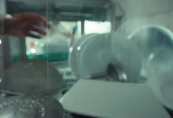 Artistic slow-motion close-up of a dishwasher rinsing plates in a commercial kitchen sink with a powerful water stream