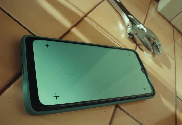 A close-up of a smartphone with a green screen and an adjustable wrench lying on a tiled floor, suggesting a repair tutorial or DIY project