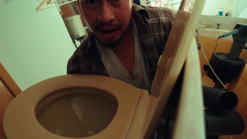 POV from inside a toilet tank shows a plumber's happy expression turn to shock and horror as he looks into the bowl