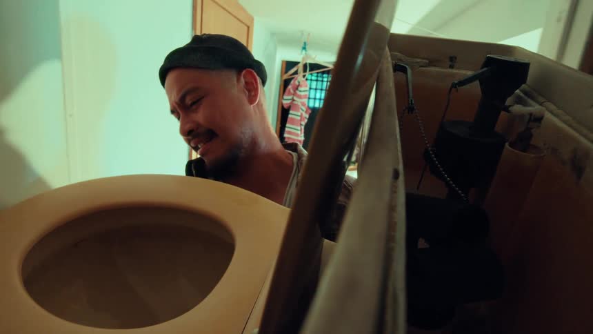 A distraught man in a beanie cries in anguish as he looks down into a toilet bowl