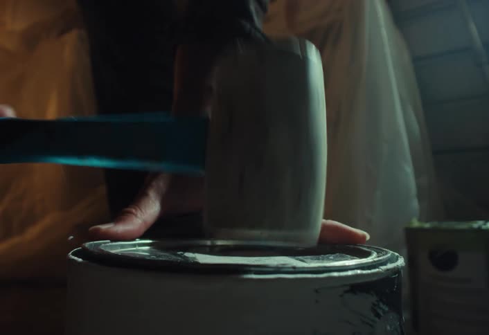 A person hammers a paint can lid shut with a rubber mallet in dramatic slow motion