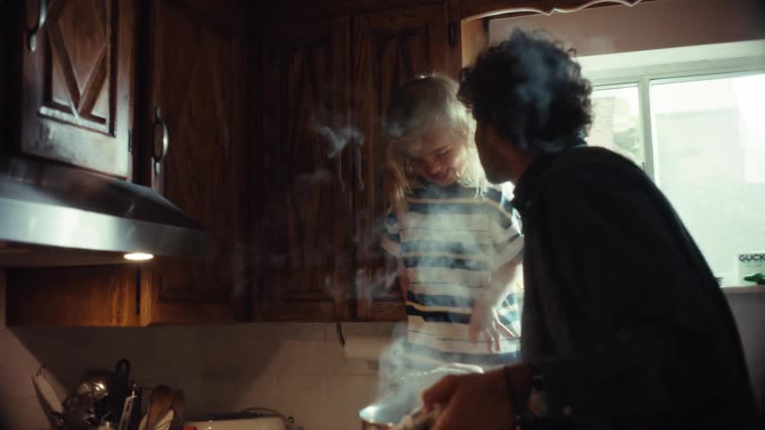 A father and his young son share a joyful moment while cooking pasta together in the kitchen