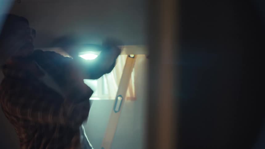 A man demolishes a wall with a sledgehammer in a dusty, backlit room during a home renovation