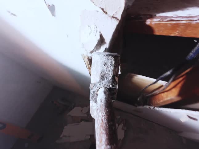First-person perspective of a sledgehammer smashing through a drywall ceiling in slow motion during a messy demolition