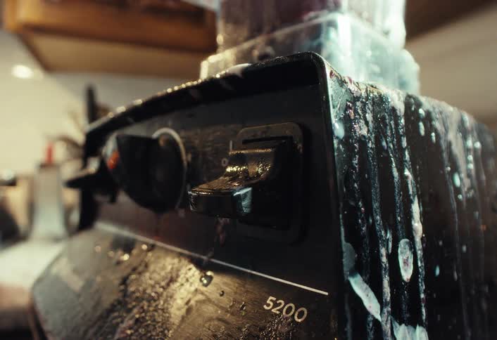 A close-up shot shows a hand turning off a messy blender covered in spillage