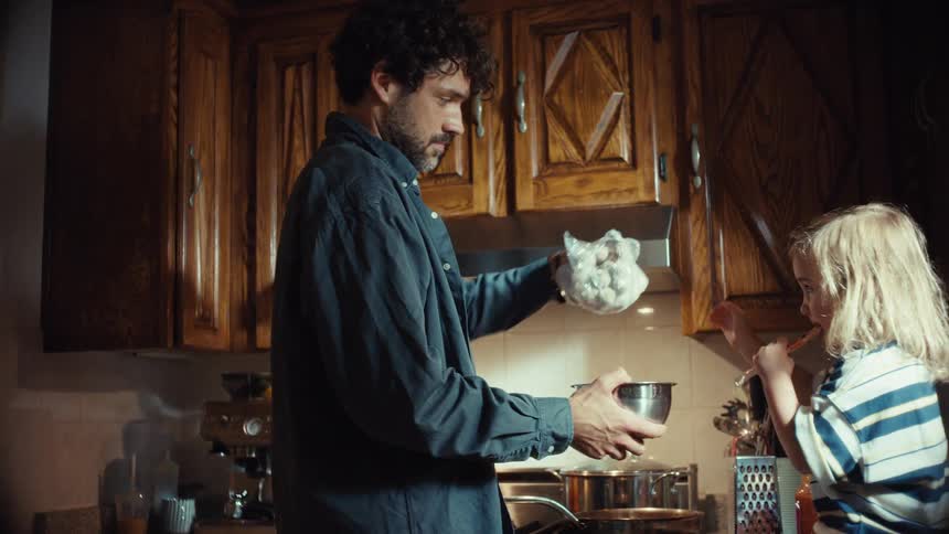 A father and his young son playfully cook dinner together in their cozy kitchen, sharing a funny and surprising moment
