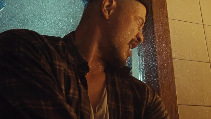 A heartbroken man cries out in anguish while getting drenched by falling water in a dramatic slow-motion close-up