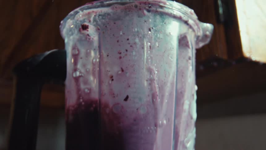 A messy purple berry smoothie overflows from a blender and drips down the side in dramatic slow motion