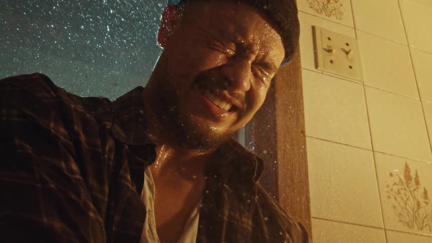 Slow motion close up shot of a heartbroken man crying in the shower with his clothes on