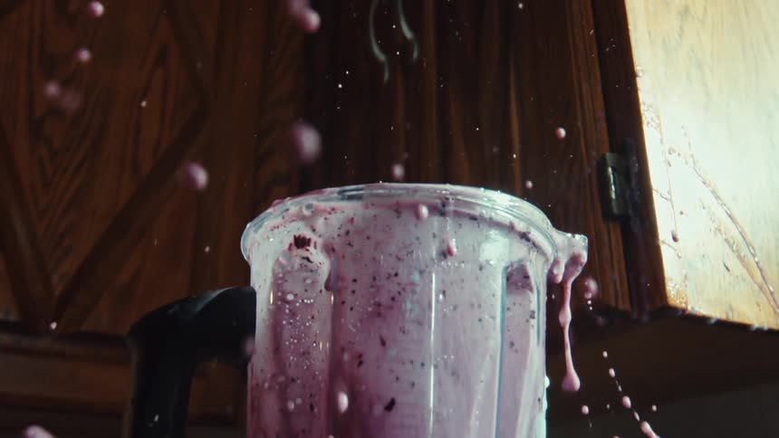 A messy blueberry smoothie explodes out of the top of a blender in super slow motion