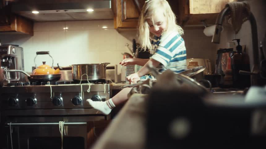 A father playfully throws dropped spaghetti at his laughing daughter in a messy kitchen after a cooking mishap