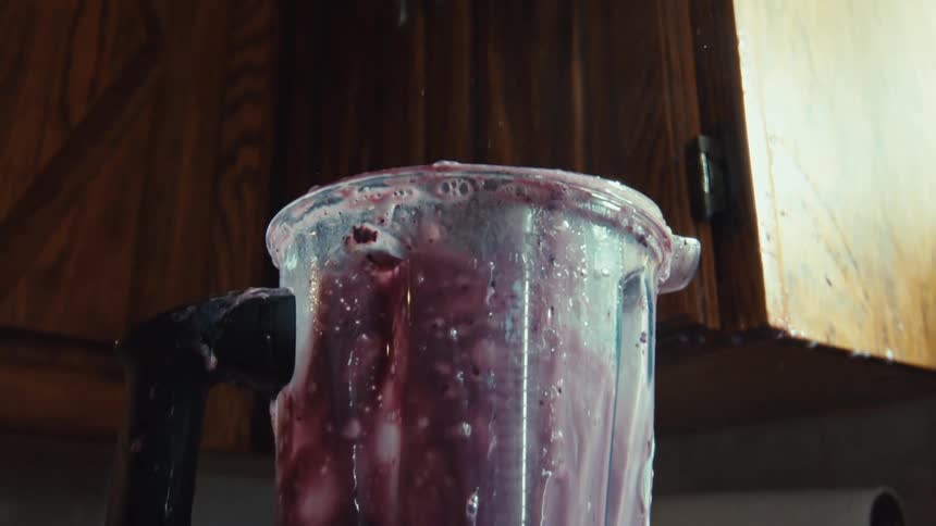 Slow motion close-up of a blender overflowing with a purple smoothie, creating a huge mess in a kitchen